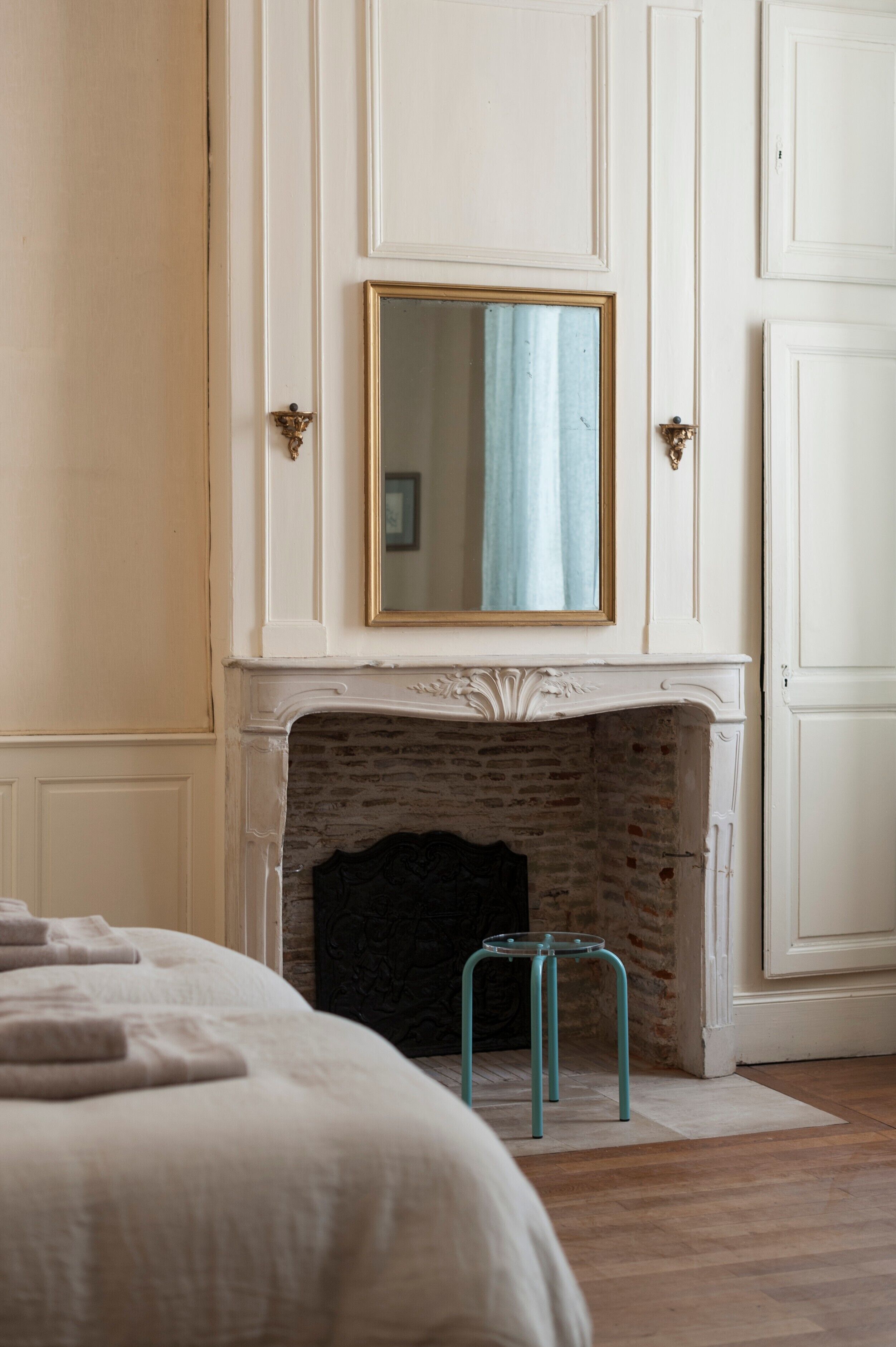 Un dormitorio con chimenea, una cama y un espejo sobre la chimenea.