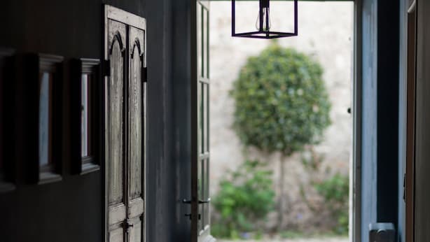 Un couloir avec un mur sombre, une porte en bois et un luminaire suspendu.