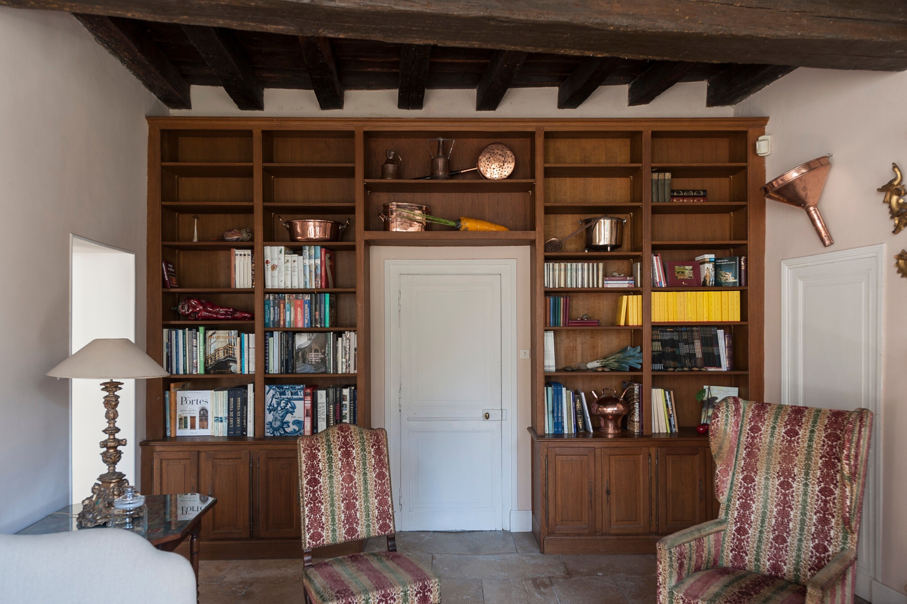 Une pièce avec une bibliothèque en bois, deux fauteuils à motifs, une porte blanche et une lampe.