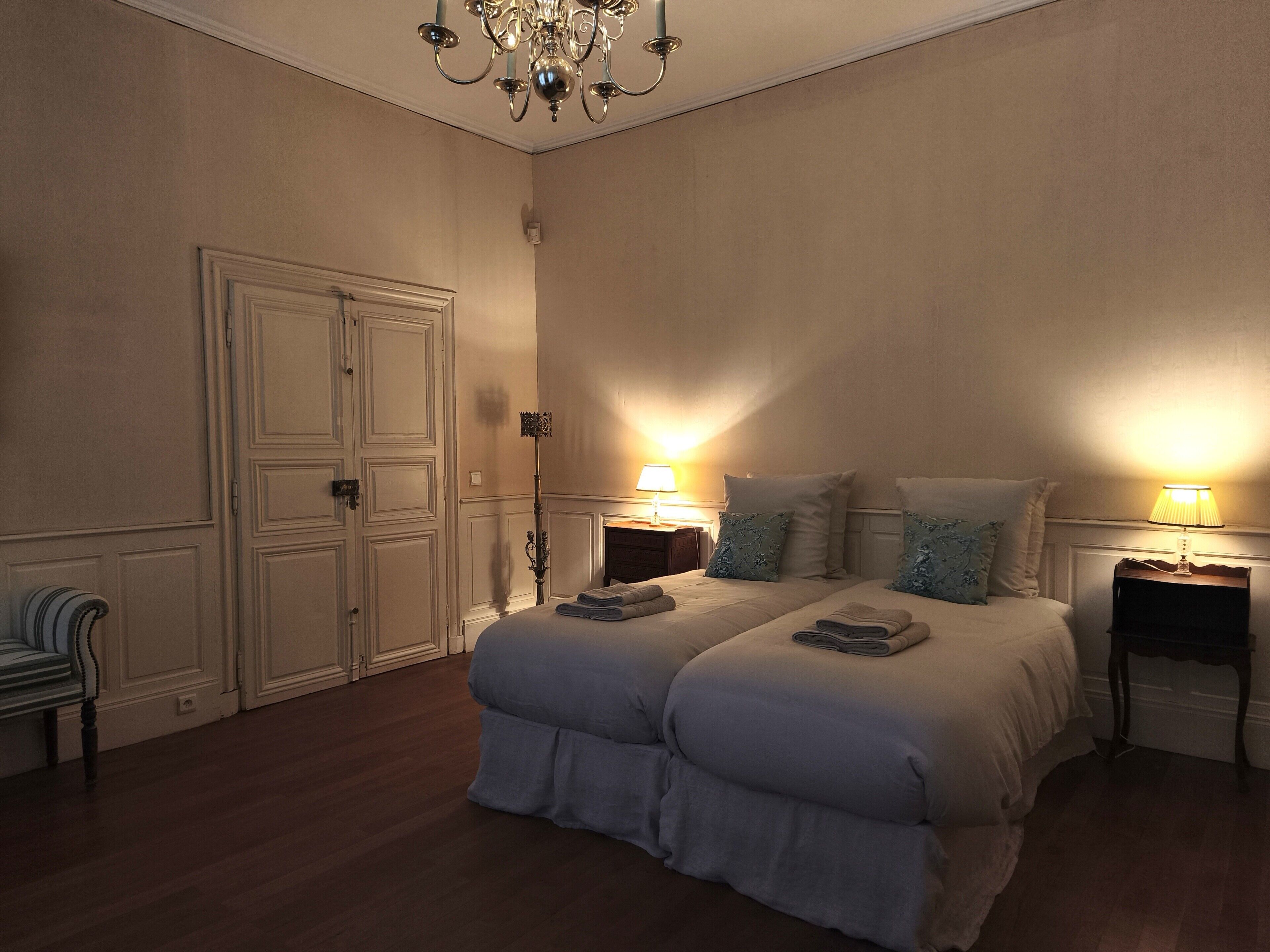 A bedroom with a double bed, two bedside tables with lamps, a chandelier, and a wardrobe.