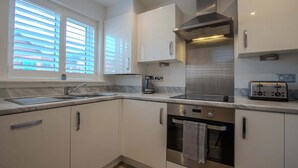 A modern kitchen with white cabinets, stainless steel appliances, and a window with blinds. - Modern 2-bed House In Swinton - Private Parking (Manchester)