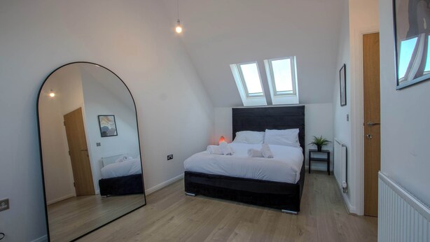 A bedroom with a bed, a large mirror, skylights, and a radiator. - Modern 2-bed House In Swinton - Private Parking (Manchester)