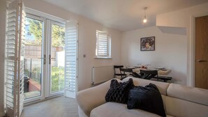 A living room with a sofa, a dining table with chairs, and a sliding glass door leading to a balcony. - Modern 2-bed House In Swinton - Private Parking (Manchester)