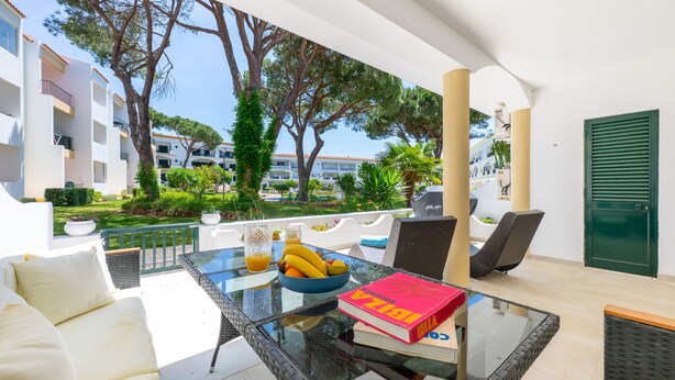 A sunlit outdoor seating area with a glass table, wicker chairs, and a bowl of fruit. - Lounge Garden Apartment (Loulé)