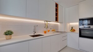 Une cuisine moderne avec des meubles blancs, un four encastré et un panier de fruits posé sur le plan de travail.