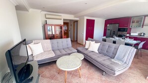 A modern living room with a grey sectional sofa, a TV, and a small round table. - Ocean View Quarteira (Loulé)