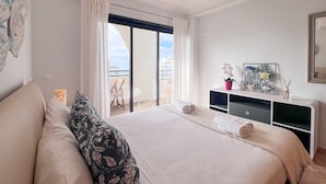 A bedroom with a large bed, a balcony with a chair, and a small table with decorative items. - Ocean View Quarteira (Loulé)