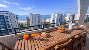 A wooden table with a view of the beach and ocean, a bowl of fruit, and a glass of orange juice on a balcony. - Ocean View Quarteira (Loulé)