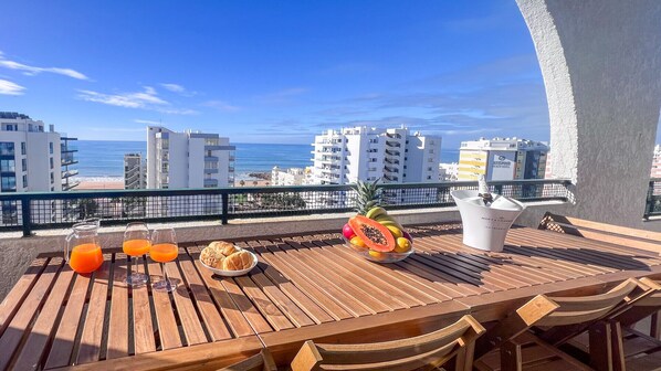 A wooden table with a view of the ocean, a pineapple, and a bottle of champagne. - Ocean View Quarteira (Loulé)