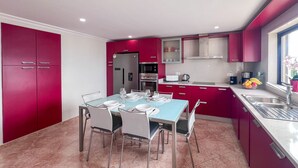 A modern kitchen with red cabinets, a blue dining table, and white chairs. - Ocean View Quarteira (Loulé)