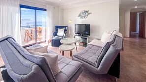 A modern living room with a sofa set, a TV, and a balcony with a view. - Ocean View Quarteira (Loulé)