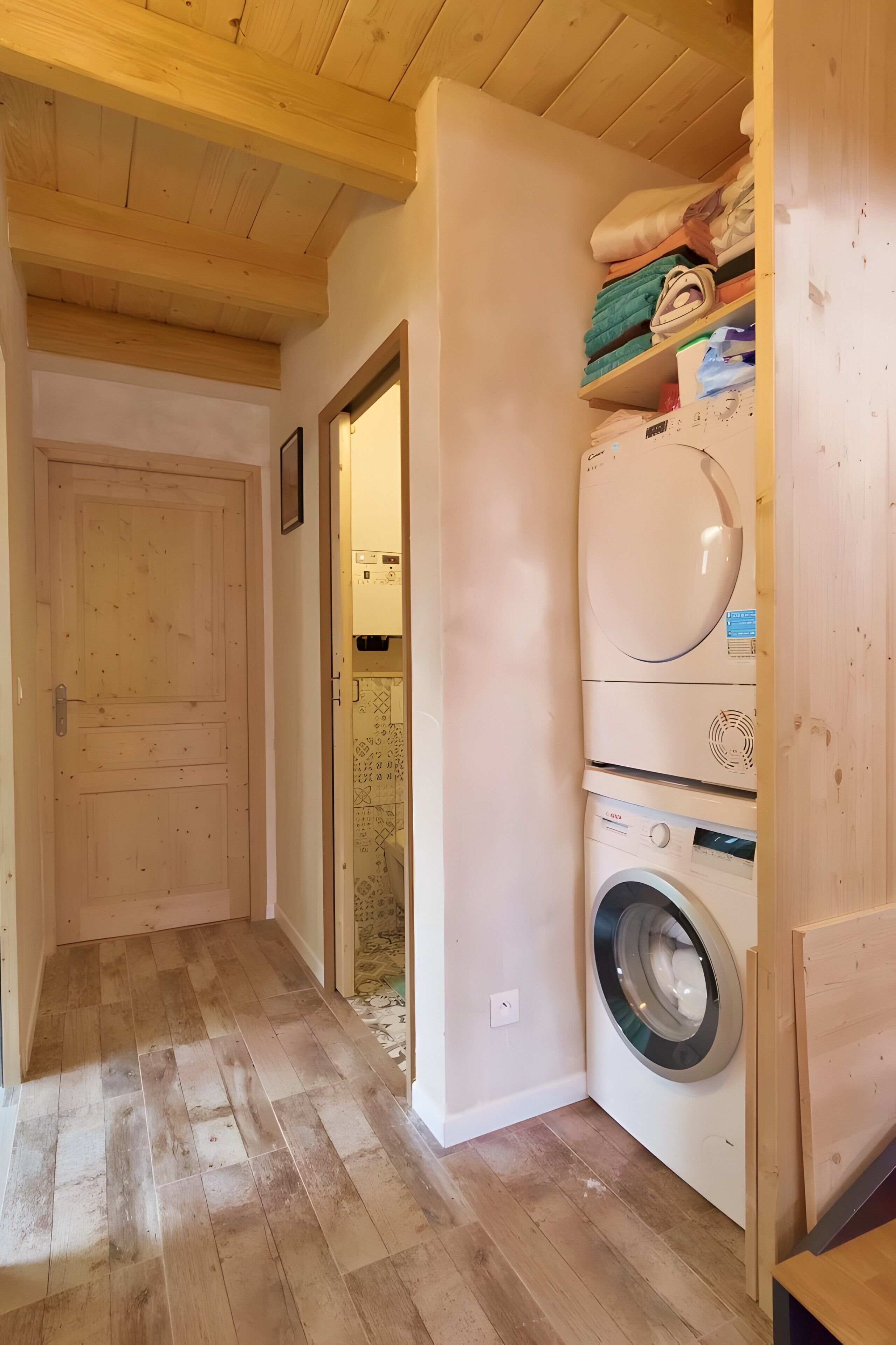 A laundry room with a washing machine and dryer, wooden flooring, and a door leading to another room.