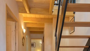 Un escalier en bois menant à un deuxième étage, un couloir avec un plancher en bois et une porte sur la gauche.