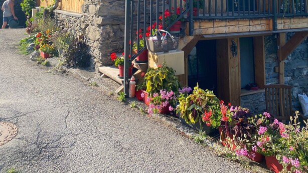 Un bâtiment en pierre doté d’un balcon en bois, de plantes en pot et d’un couvercle d’accès à une bouche d’égout.