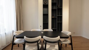 Un comedor con una mesa negra y seis sillas, una estantería y una ventana con cortinas.