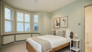 A bedroom with a wooden bed, white bedding, a bedside table with a lamp, and two framed pictures on the wall. - The Fulham Patio Apartment (London)