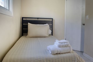A neatly made bed with a headboard, a window, and a door in the background.