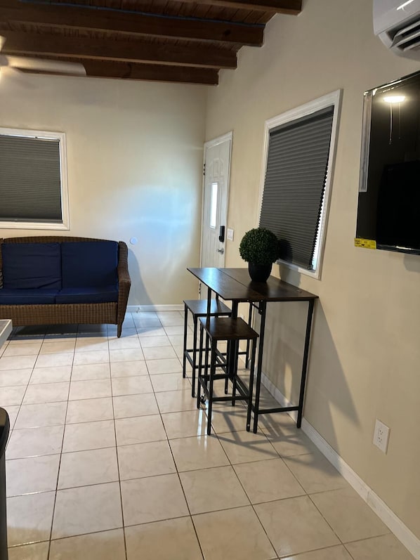 A room with a dark blue sofa, a small table with a potted plant, and a TV mounted on the wall.