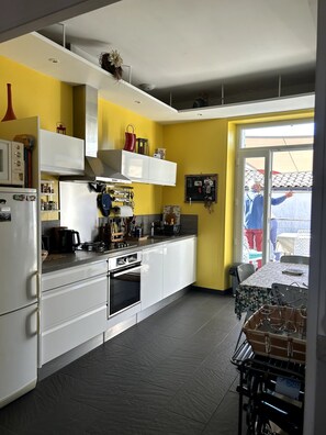 Une cuisine avec des meubles blancs, une cuisinière et un four à micro-ondes. Il y a une fenêtre donnant sur un balcon.