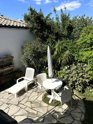 A patio with white chairs and a table, surrounded by greenery and a tiled roof. - Fisherman’s House with Private Garden – Comfort & Privacy in Pornic (Pornic)
