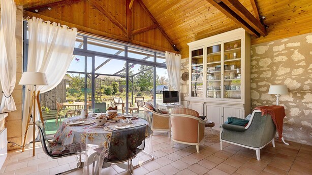 Un patio cubierto con una mesa de comedor, sillas, un televisor y un mueble con puertas de vidrio.