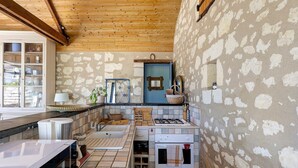 Una cocina con pared de piedra, vigas de madera en el techo, una puerta azul y suelo de baldosas.
