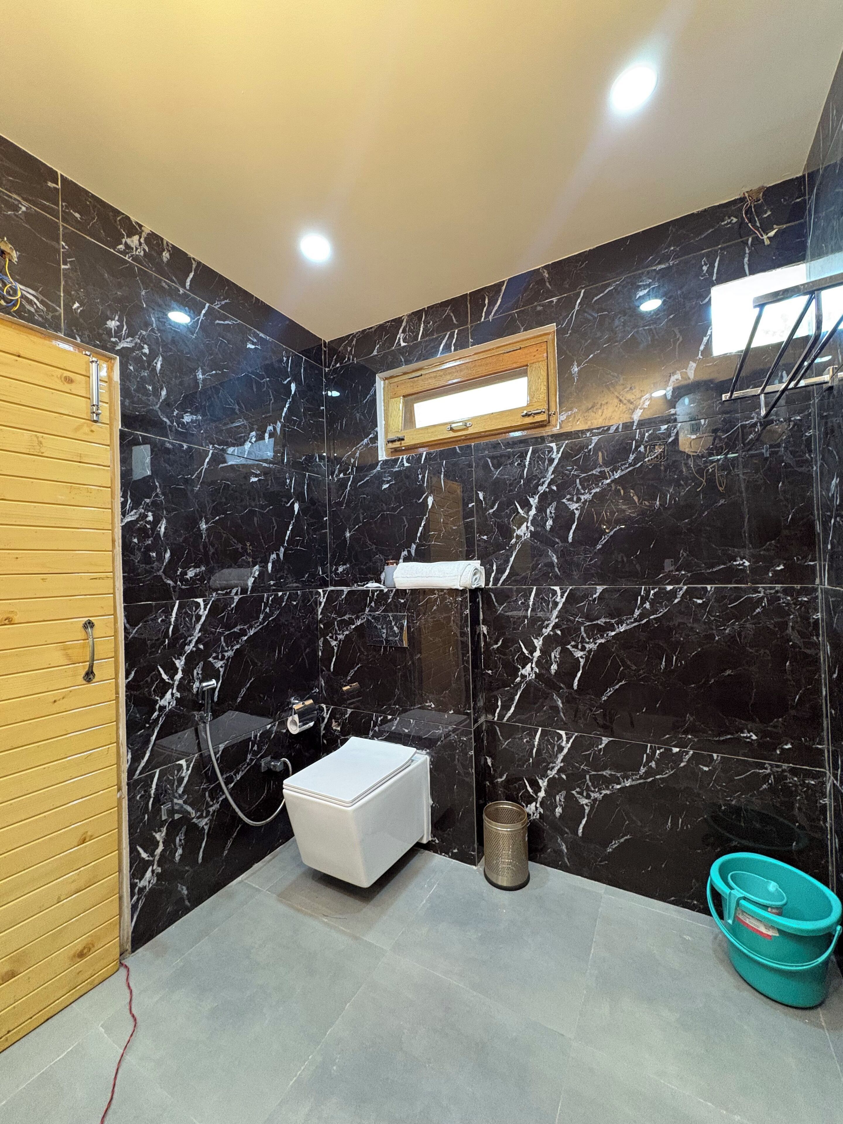 A bathroom with black marble walls, a wooden door, a white toilet, a sink, and a window.