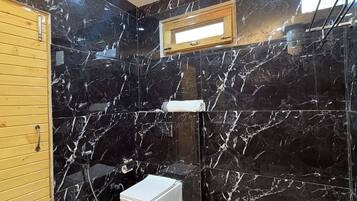 A bathroom with black marble walls, a wooden door, a white toilet, a sink, and a window.