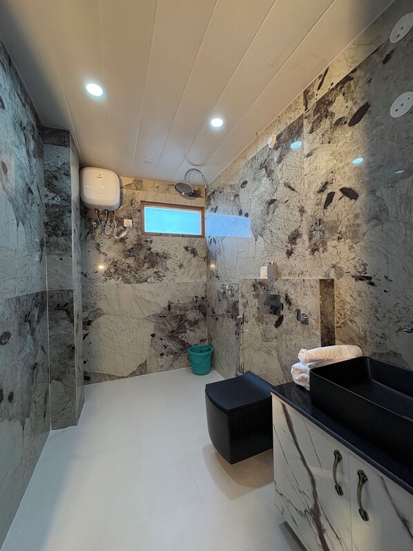 A bathroom with a marble wall, a black sink, a window, and a shower.