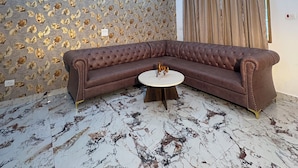 A living room with a brown sectional sofa, a round coffee table, and a patterned wallpaper. - SECRET ESCAPE RESORT (Solan)