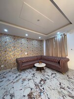 A living room with a brown sectional sofa, a round coffee table, and a patterned wallpaper.