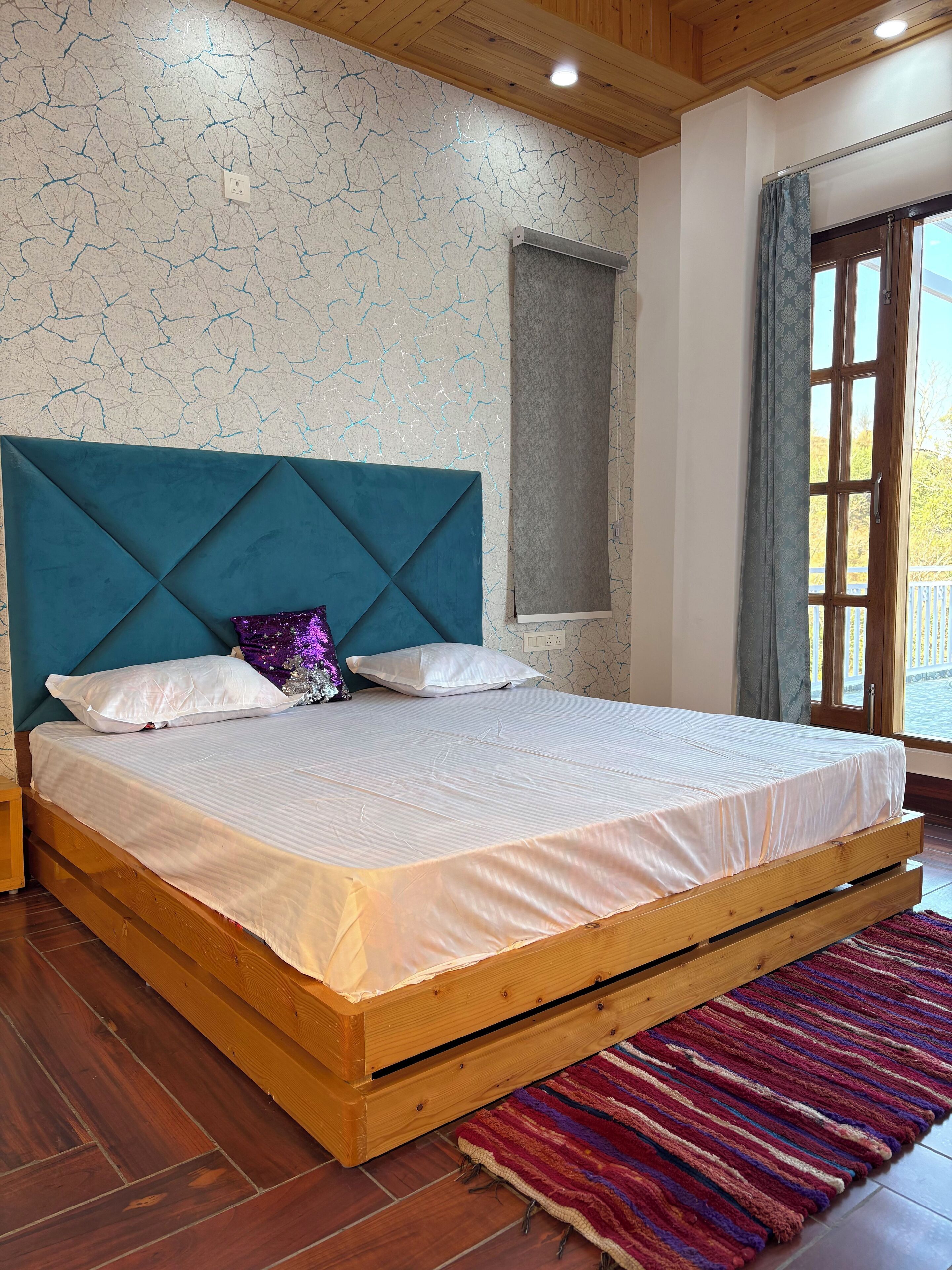 Ein Schlafzimmer mit einem hölzernen Bettgestell, weißer Bettwäsche, einem türkisblauen Kopfteil und einem farbenfrohen Streifen Teppich.