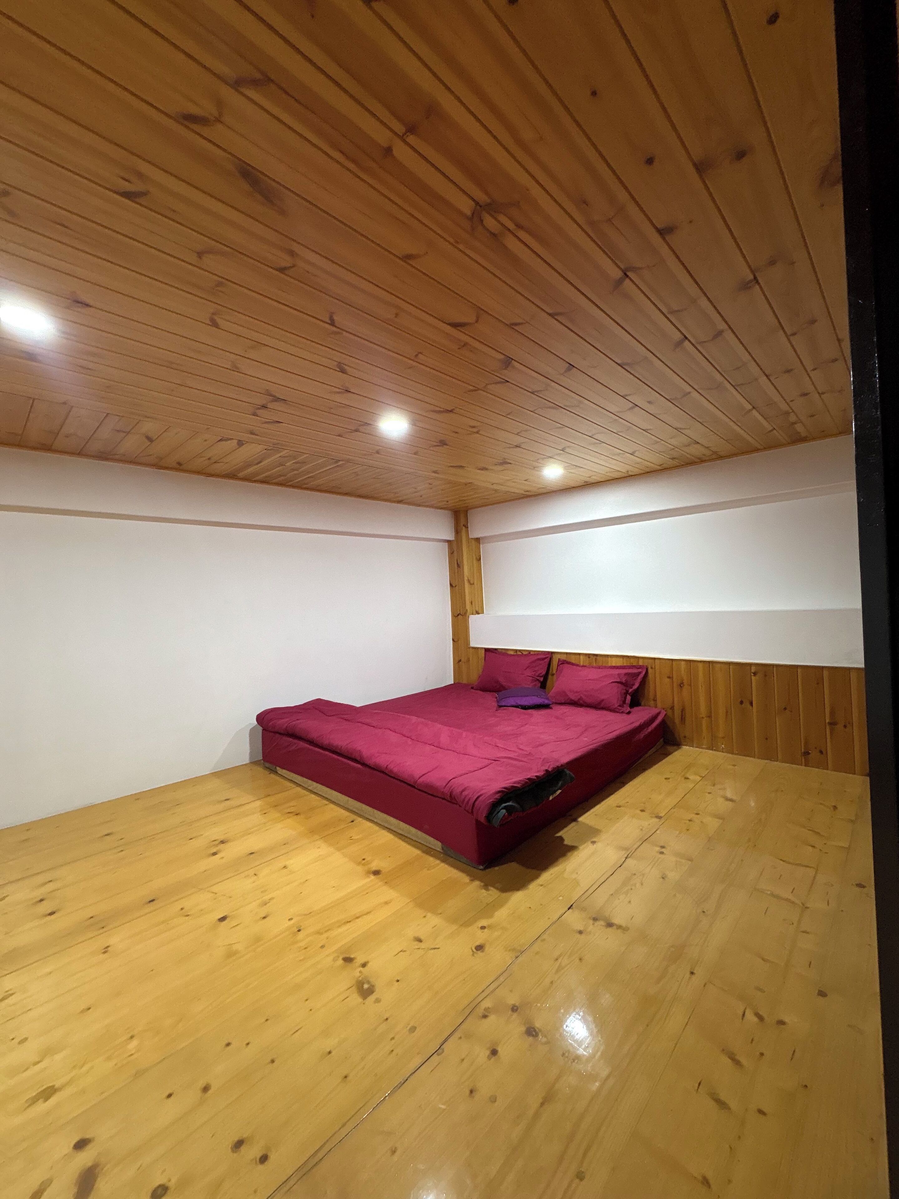 A bedroom with a wooden ceiling, a bed with a red bedspread, and a white headboard.