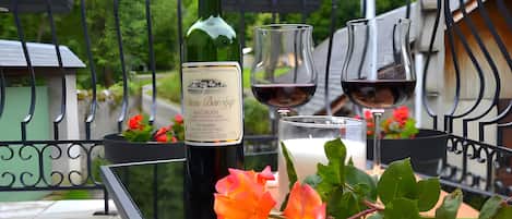 A balcony with a table set for two, featuring a bottle of wine, two glasses, and a candle.