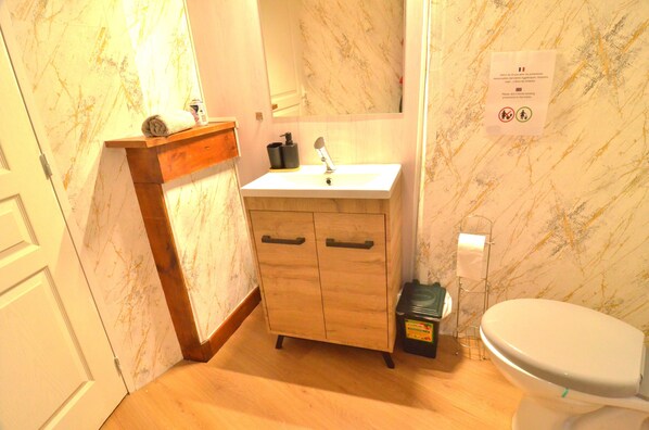 Une salle de bain avec un mur en marbre, un meuble en bois, un lavabo et des toilettes.