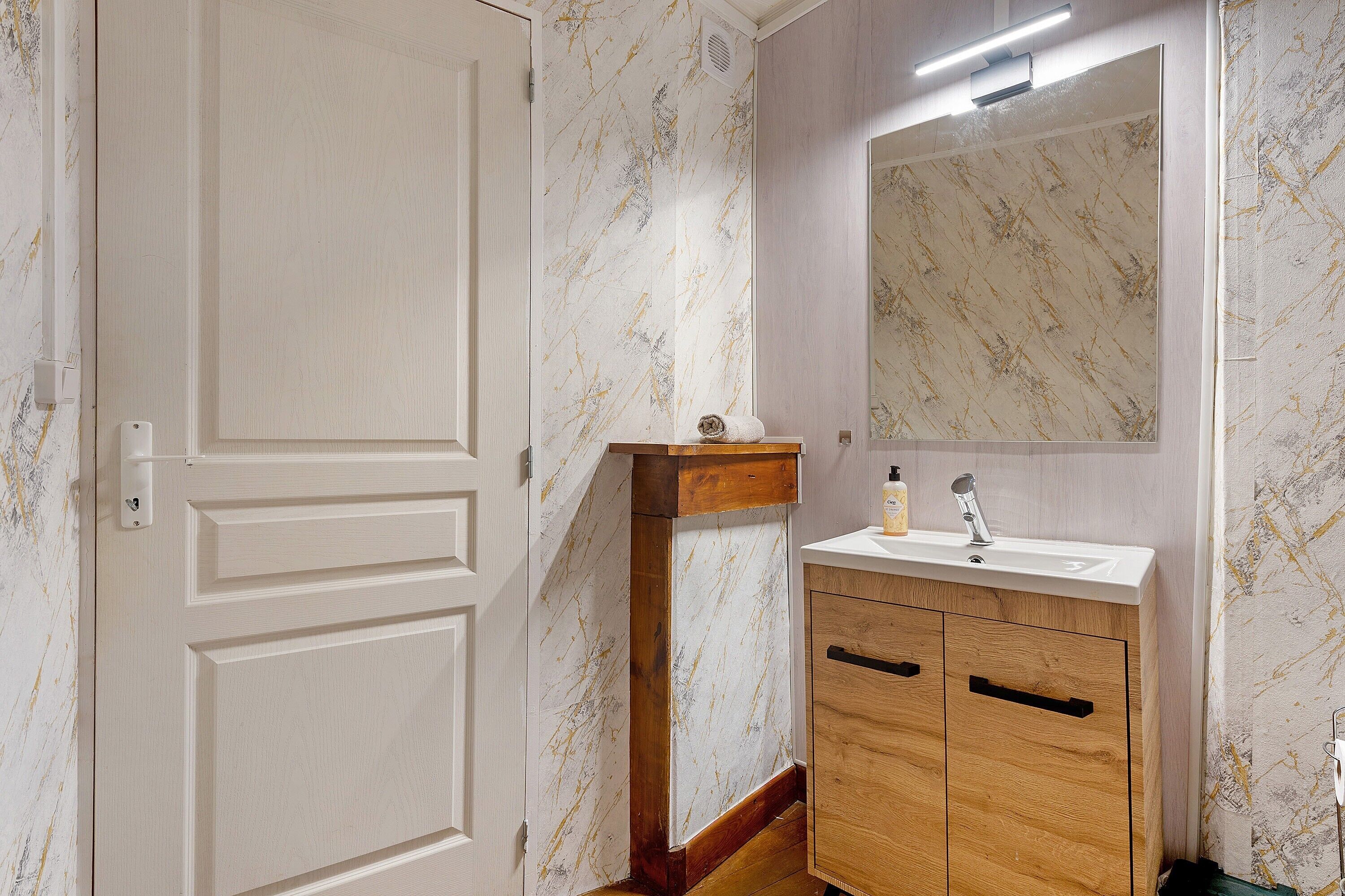 Un baño con pared de diseño marmolado, tocador de madera con lavamanos y un espejo sobre el tocador.