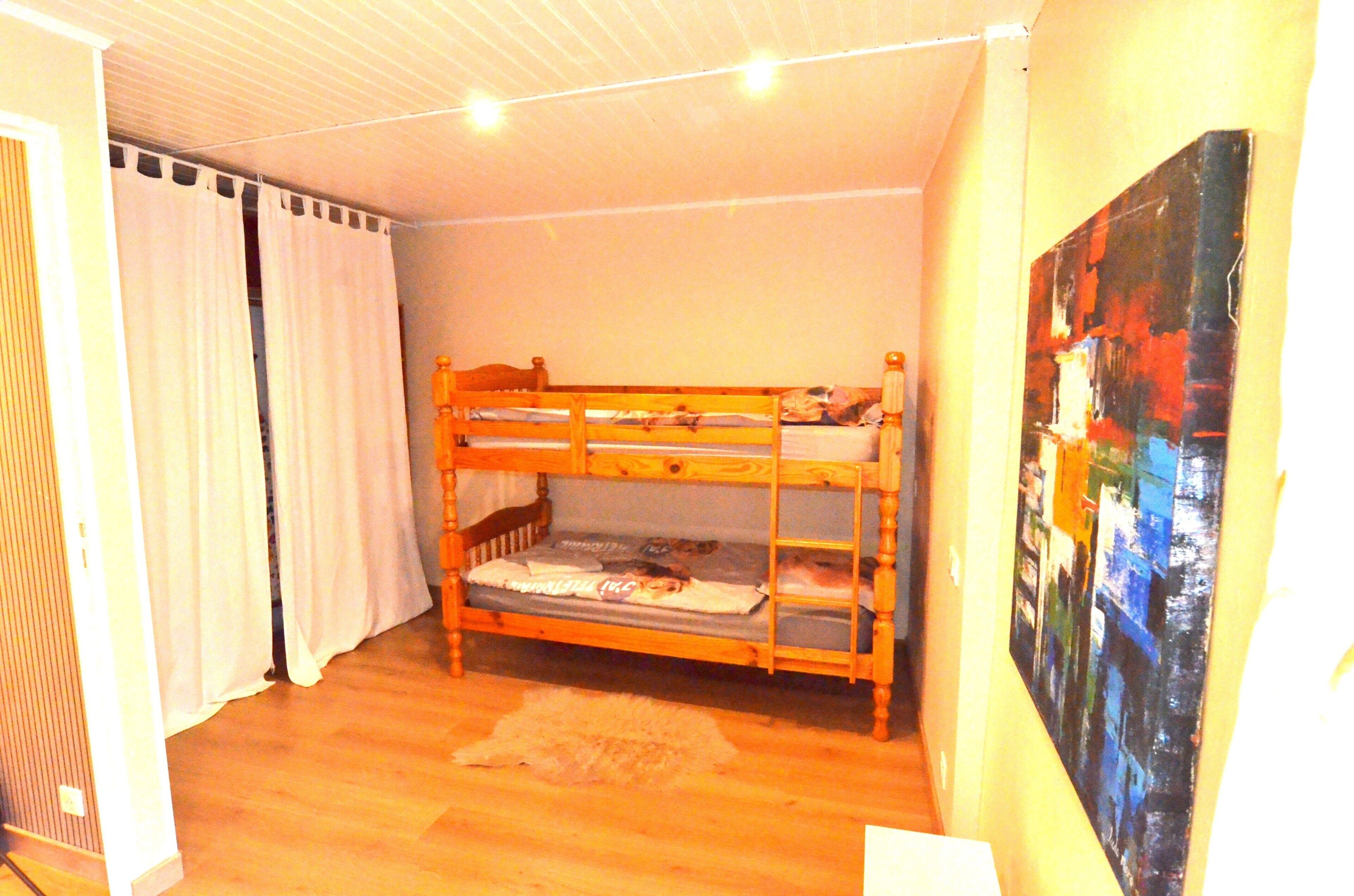 A bunk bed room with a painting on the wall, a curtain, and a rug on the floor.