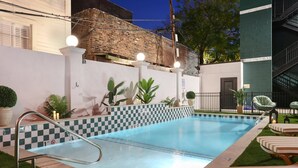 Una piscina con borde de baldosas a cuadros, una escalera metálica y sillas de descanso.