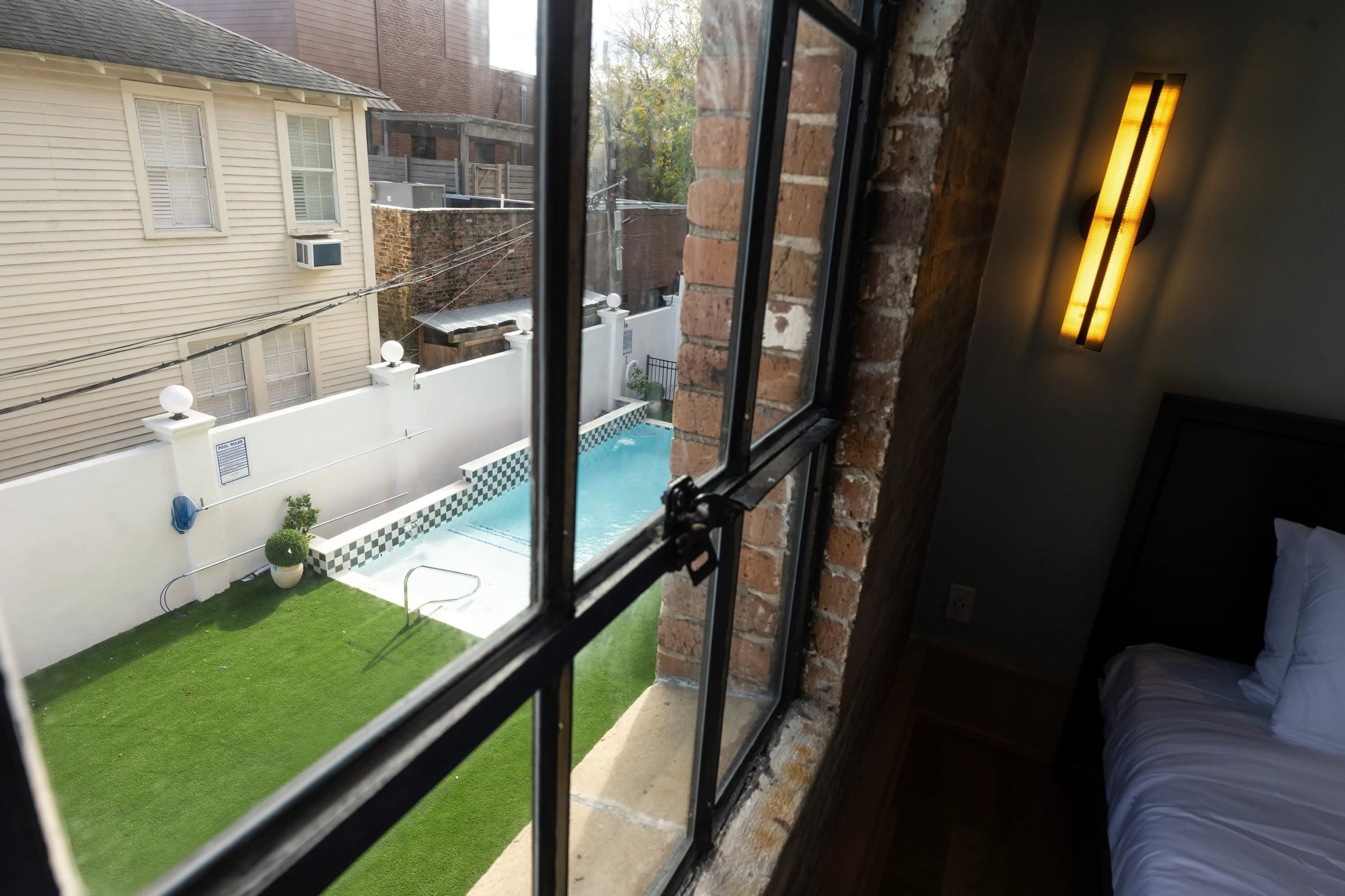 Una habitación con un amplio ventanal que da a un patio trasero con piscina, un pequeño jardín y una valla blanca.
