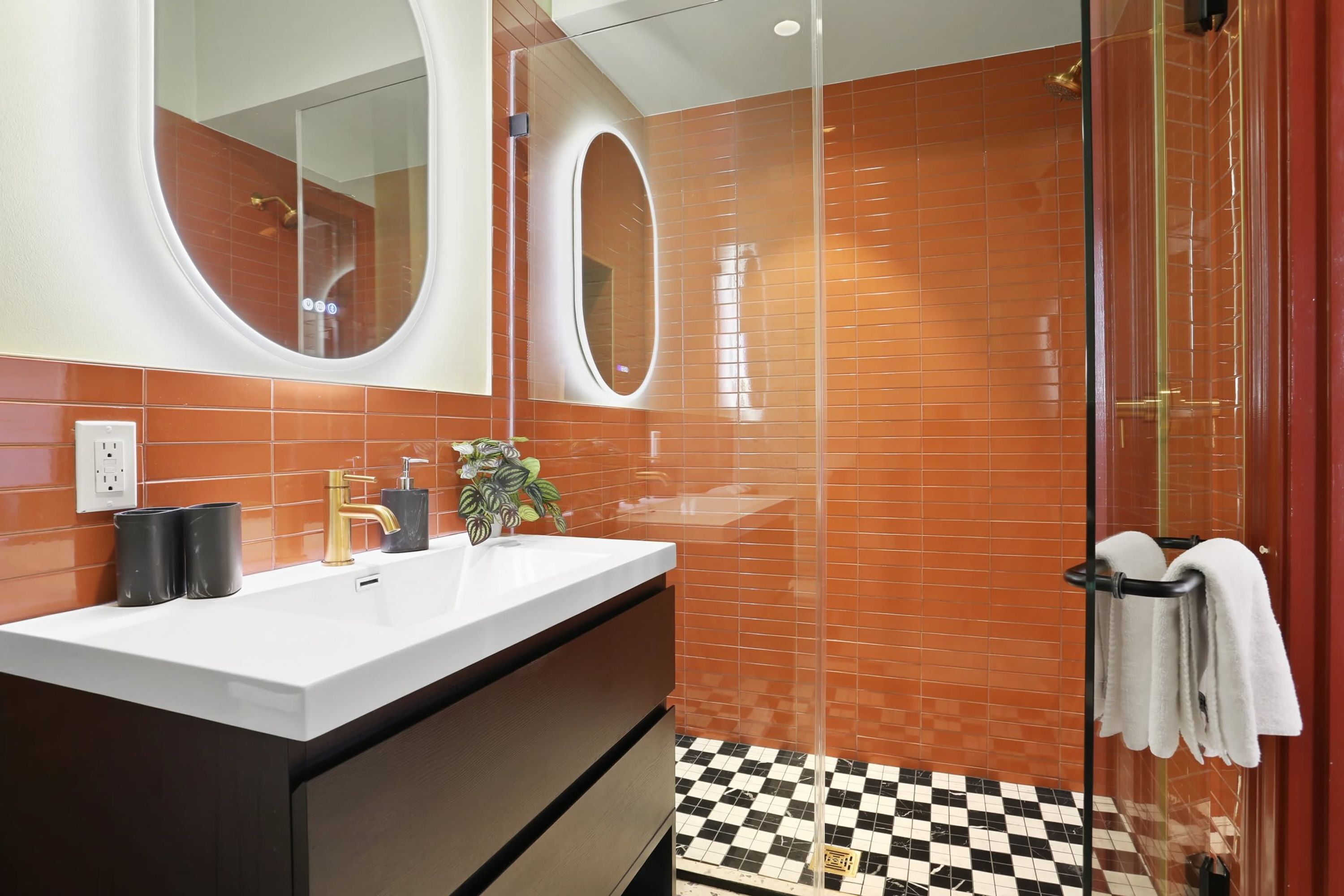 A modern bathroom with a white sink, two black soap dispensers, a gold faucet, and a potted plant.