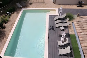 Une piscine rectangulaire dotée d’une terrasse en bois et de chaises longues.
