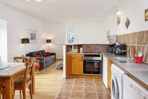 A compact kitchen with a washing machine, oven, and a dining area with a table and chairs. - "Petit Gîte" with Private Terrace, Mountain View, Shared Pool (Saint-Jean du Gard)