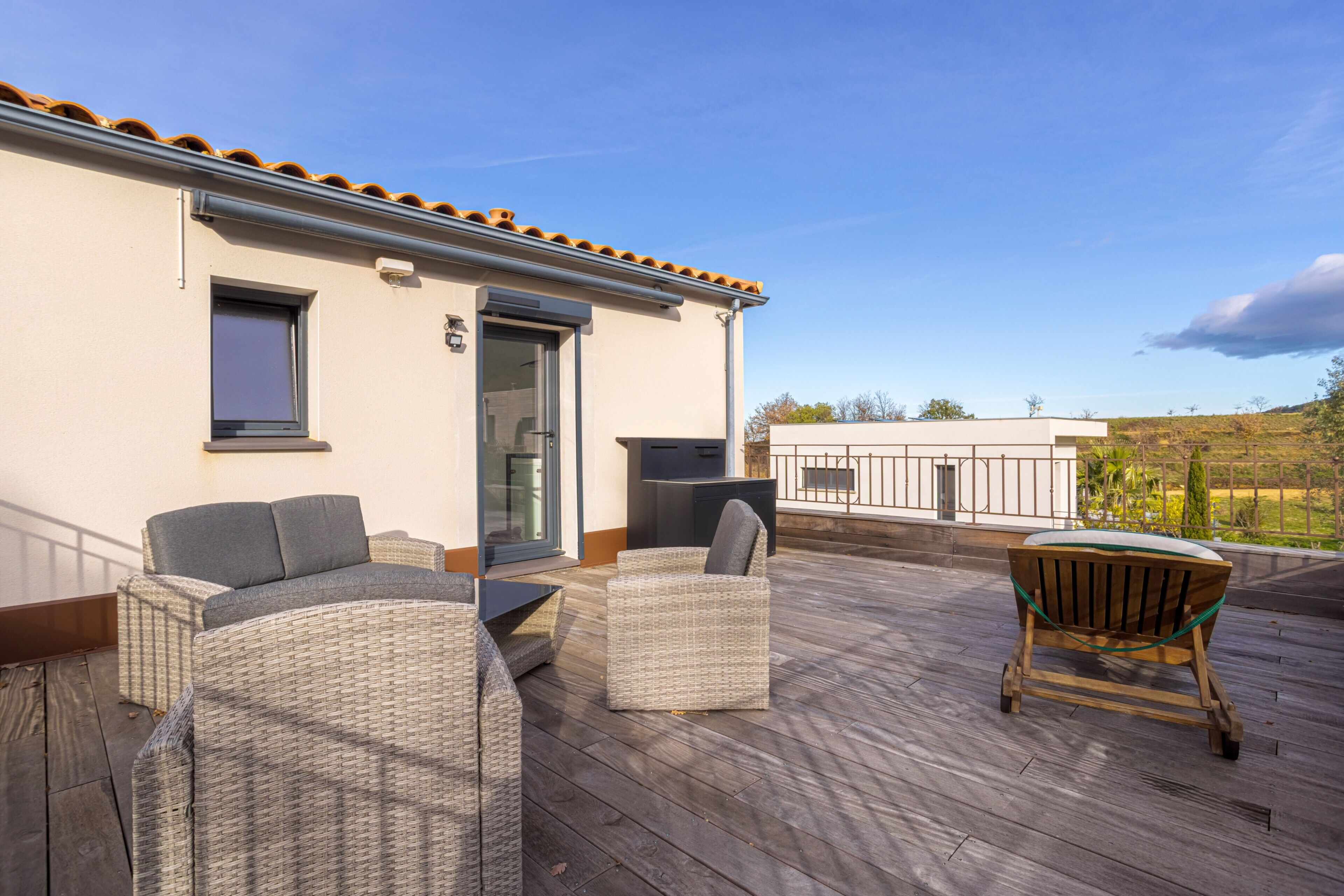 Un espace extérieur abrité, aménagé avec des meubles en osier, un barbecue et offrant une vue sur le paysage environnant.