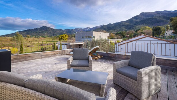A rooftop patio with wicker furniture, a glass table, and a view of mountains.