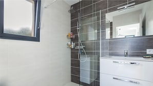 A modern bathroom with a shower, a sink with a mirror, and a window.