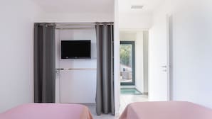 A hotel room with two beds, a TV, a balcony, and a door leading to an outdoor area.