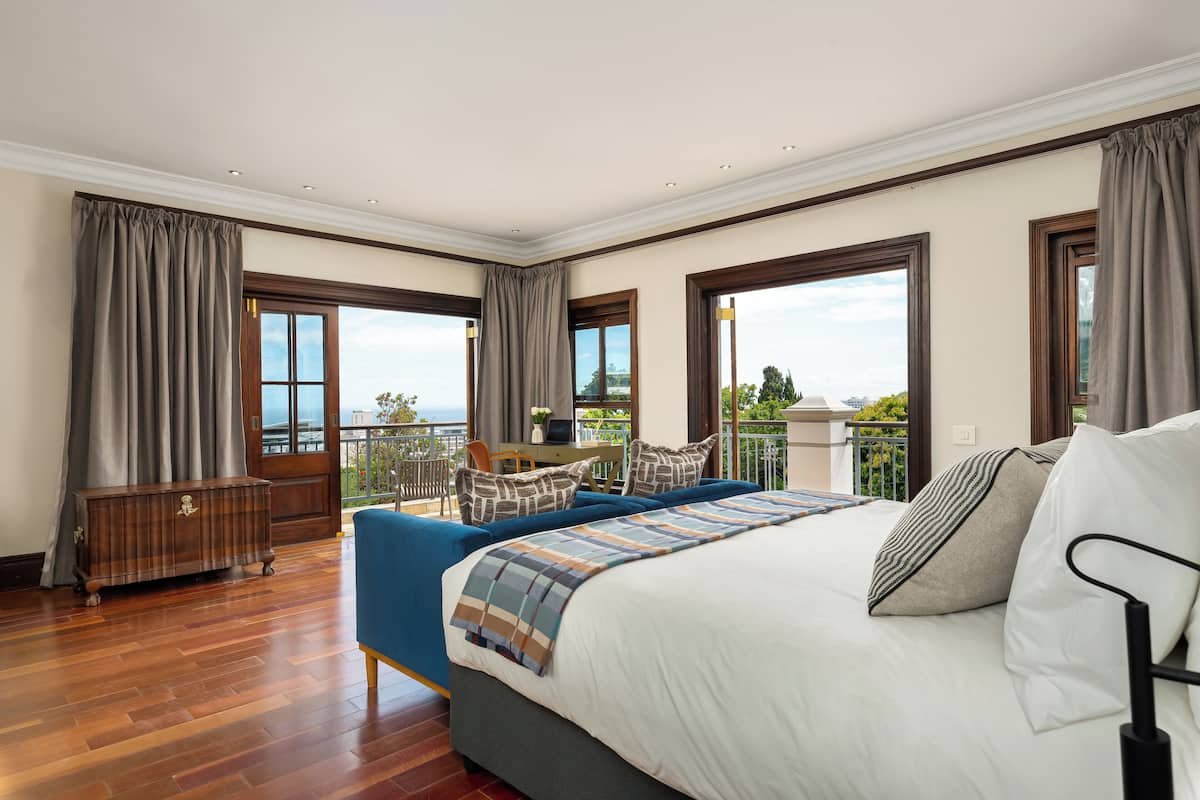 Une chambre d’hôtel avec un grand lit, un canapé, une commode en bois et un balcon avec vue.