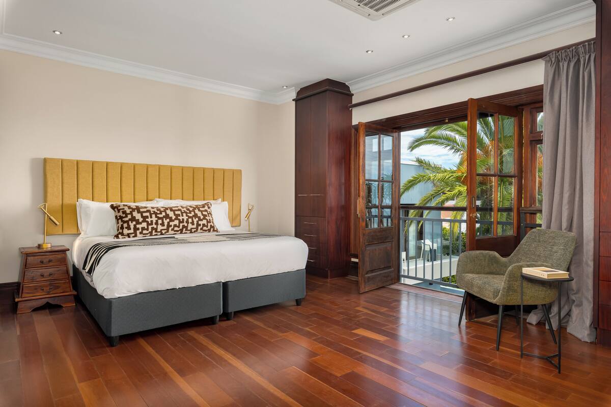 Une chambre d’hôtel avec un grand lit, un plancher en bois, une chaise et un balcon donnant sur des palmiers.