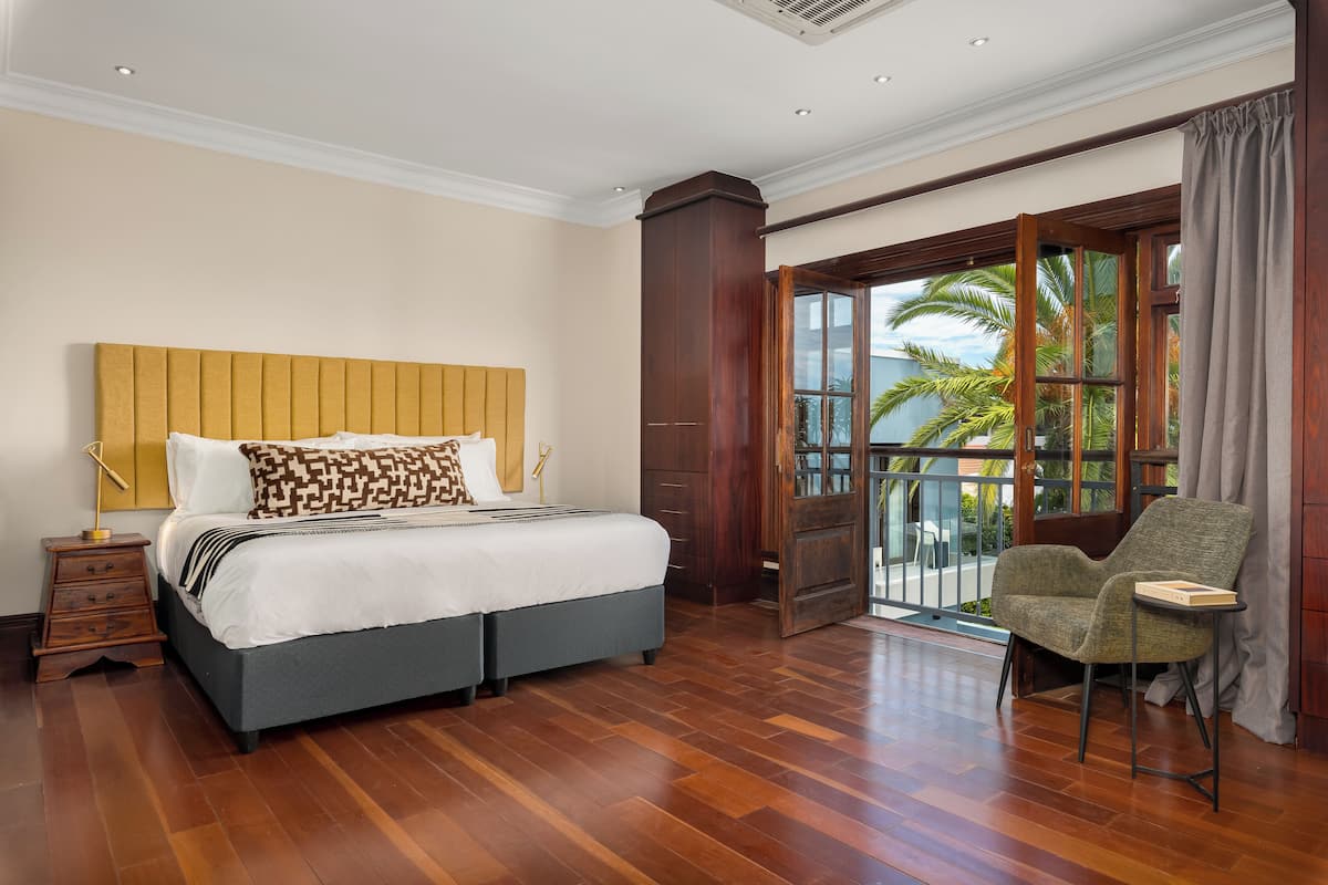 Une chambre d’hôtel avec un grand lit, un plancher en bois, une chaise et un balcon donnant sur des palmiers.