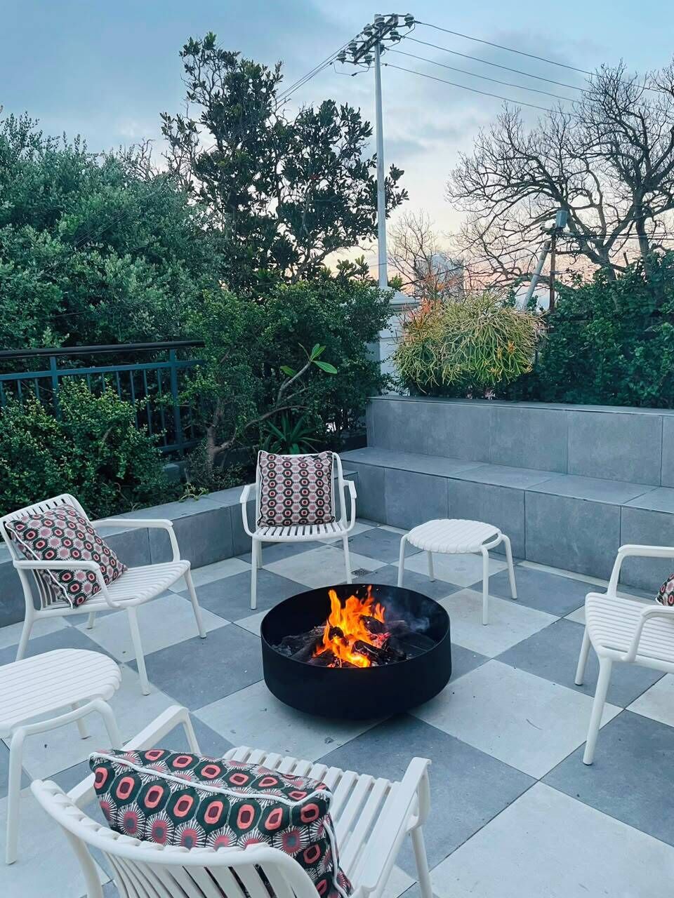 Een terras met witte stoelen en een zwarte vuurkorf.